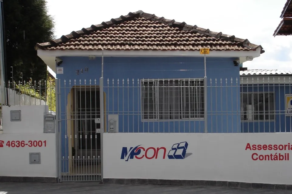 Fachada azul da MPCon em 2005, com o muro pintado com o logo antigo, o telefone 4636-3001 e a frase Assessoria Contábil